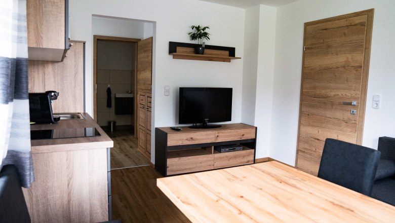Modern living room with wooden furniture, TV and kitchen.