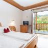 A cozy double room with wooden furniture, a balcony with a view of the countryside and a small TV.