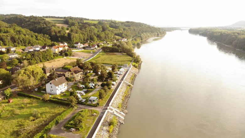 Aerial view of a riverbank with houses and mobile homes, surrounded by green countryside.