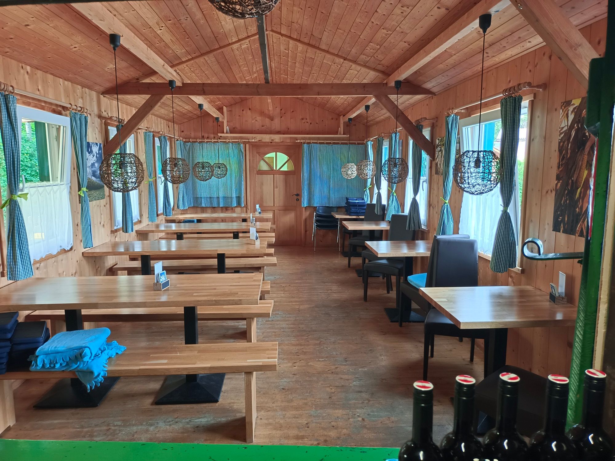 Interior view of a rustic dining room with wooden tables and benches, decorative lamps and curtains.