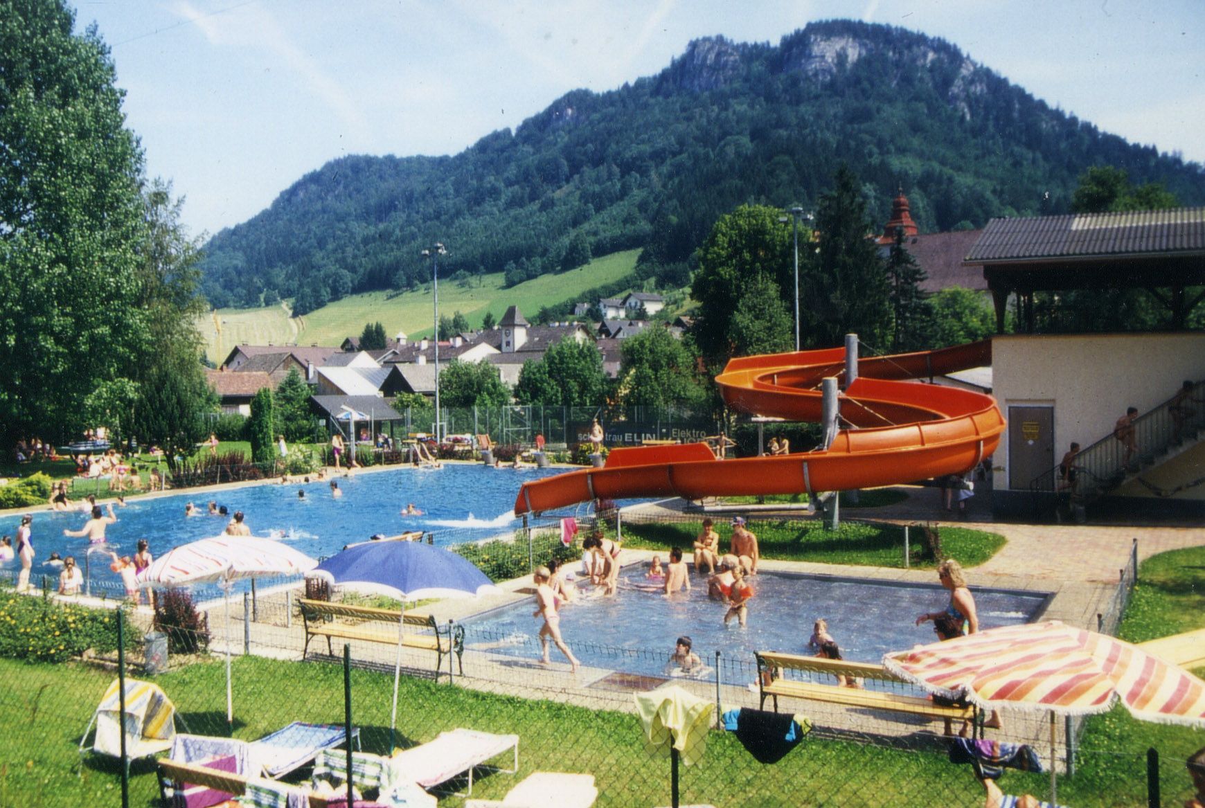 Outdoor pool with slide and mountain landscape in the background.