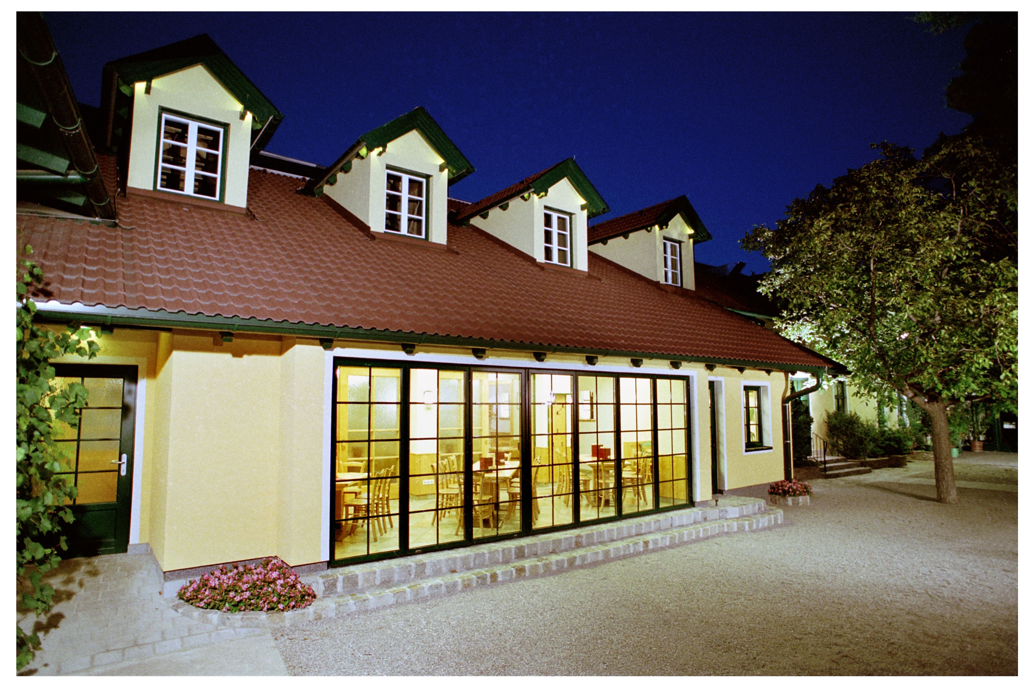 A building with a yellow façade and red roof tiles at night, illuminated from the inside.