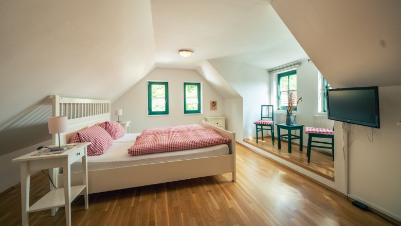 Cozy bedroom with wooden floor, double bed, bedside tables, two chairs and a TV on the wall.