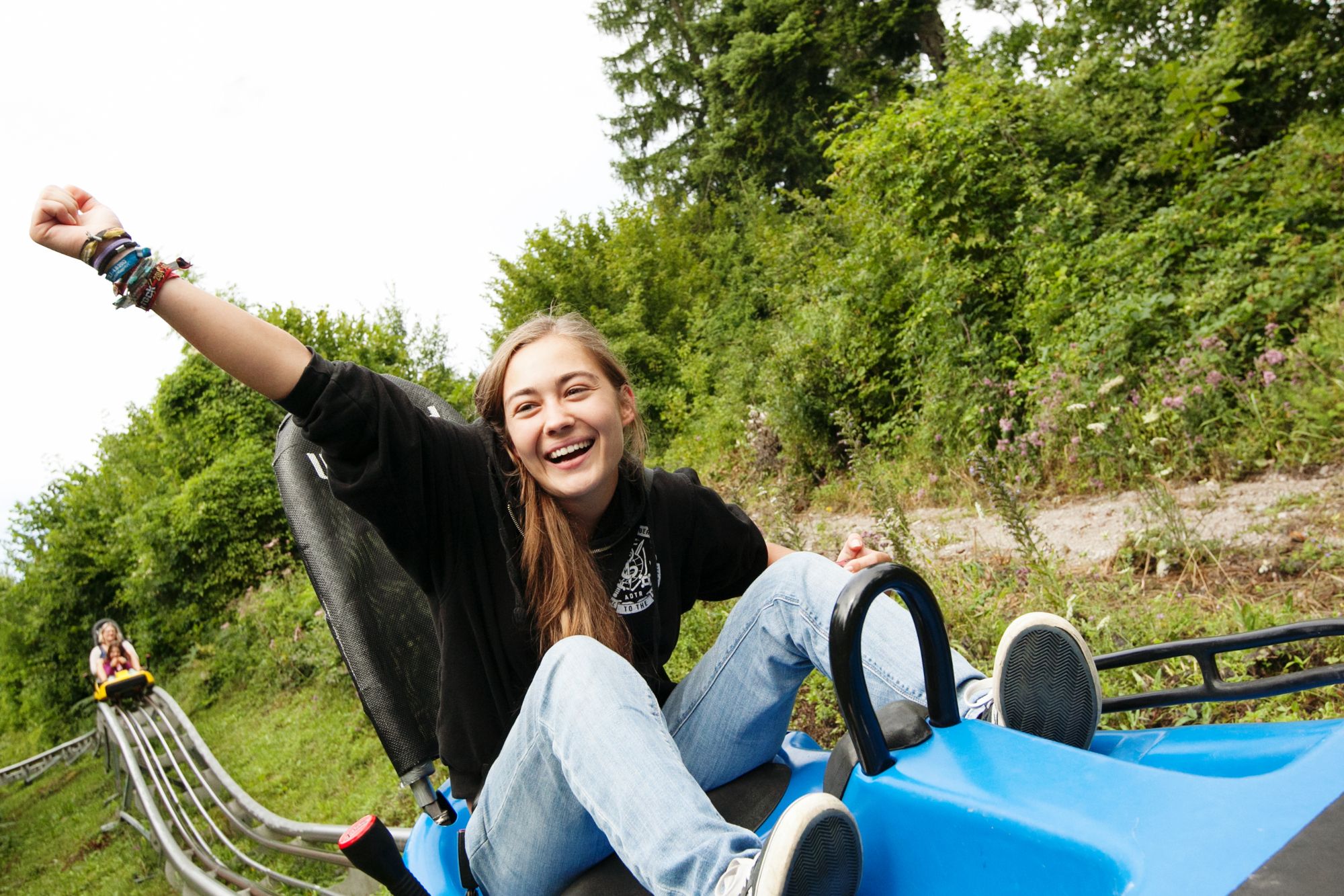 A smiling person rides on a summer toboggan run, surrounded by green nature.