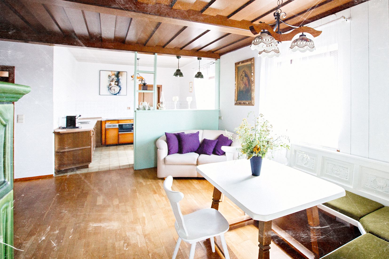 A cozy living room with a wooden floor, a sofa, a dining table, and a kitchen in the background.