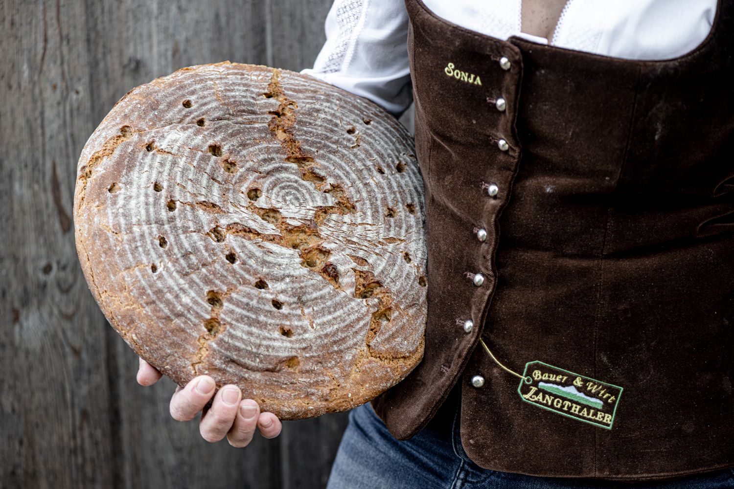 Person holds round, home-baked bread in front of a rustic background.