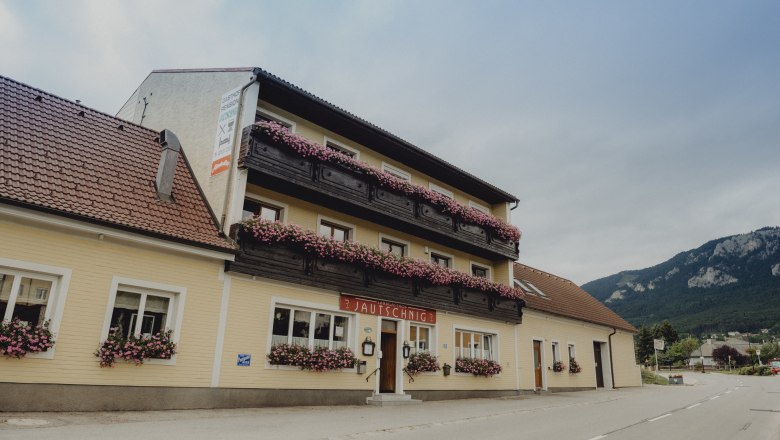 A traditional country inn with balconies decorated with flowers against a mountain backdrop.