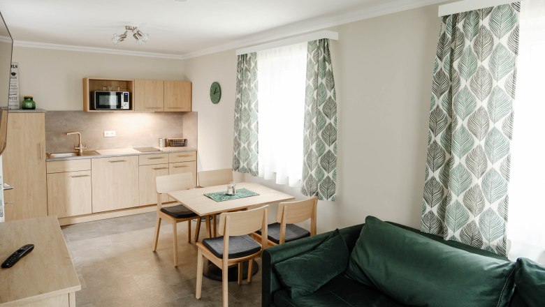 Modern kitchen with wooden furniture, dining table, green curtains and sofa.