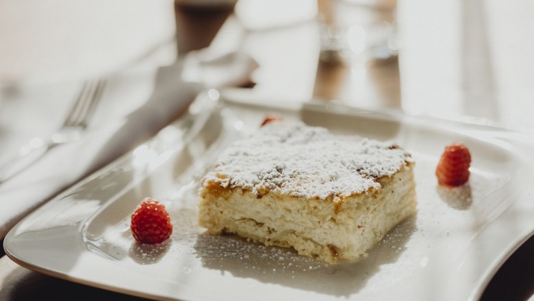 A piece of milk cream strudel with powdered sugar and raspberries on a white plate.