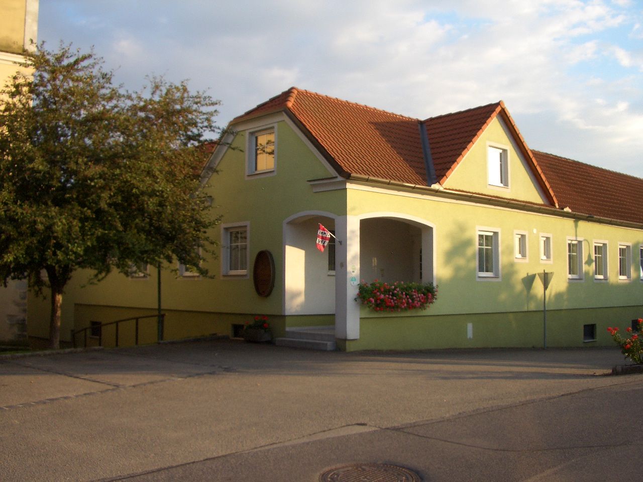 Yellow building with a red roof and flowers at the entrance.
