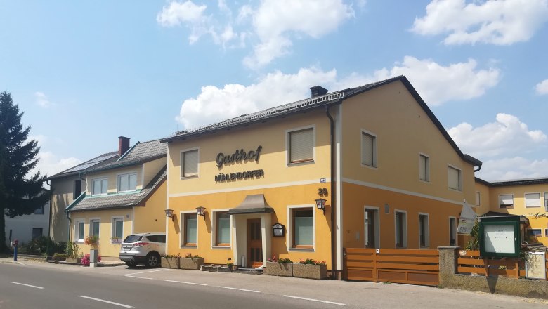 A yellow building with the inscription 'Gasthof M&uuml;hlendorfer' on a street.