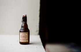 A bottle of RaxBräu Helles Bier on a white surface against a dark background.