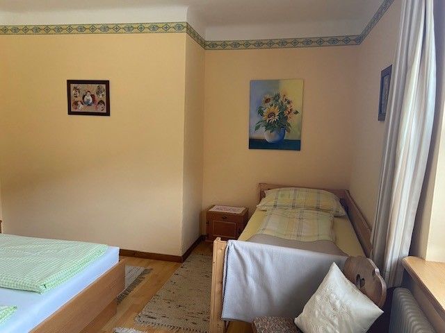 A room with two beds, a single bed and a double bed, decorated with pictures of flowers on the walls.