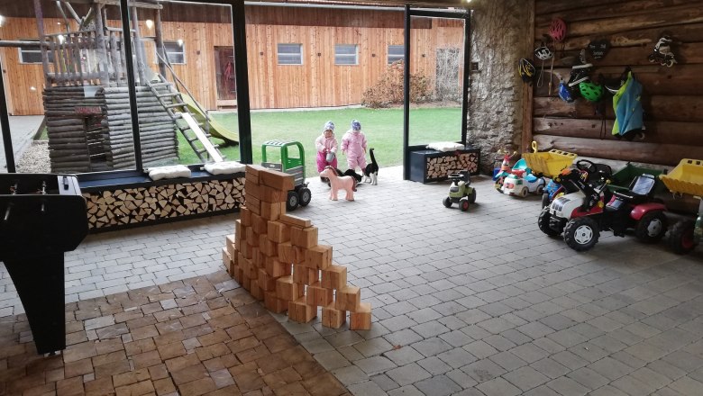 Interior view of a play barn with toy cars, wooden blocks and two children in winter clothing.