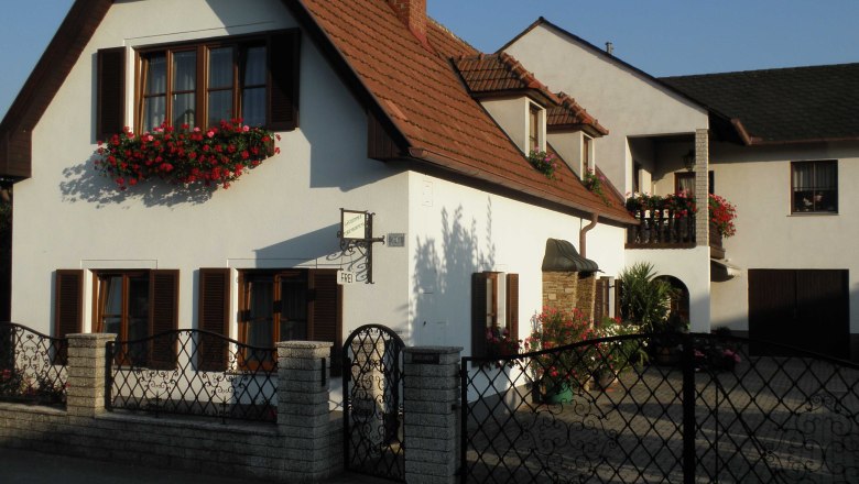 House view, © Helga Schweigl A two-storey house with white walls, red roof tiles and flower boxes in front of the windows.