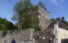 Historic stone wall and tower in Drosendorf-Zissersdorf, surrounded by trees and blue sky.