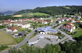 Aerial view of a village with community center and surrounding houses in a green hilly landscape.