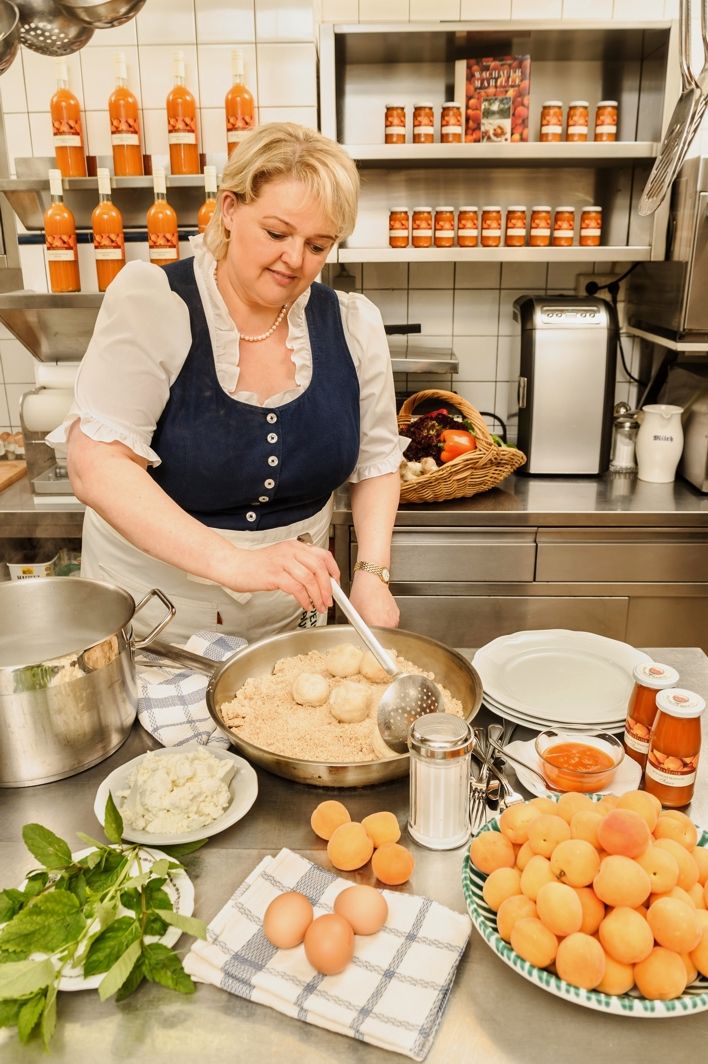 Woman in traditional dress cooking in a kitchen with regional ingredients.