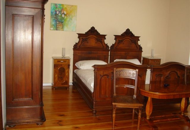 A traditionally furnished bedroom with antique wooden furniture, including two beds, a wardrobe and a table.