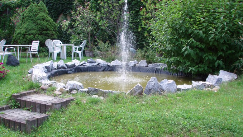 Garden with small pond and fountain, surrounded by plants and garden furniture.
