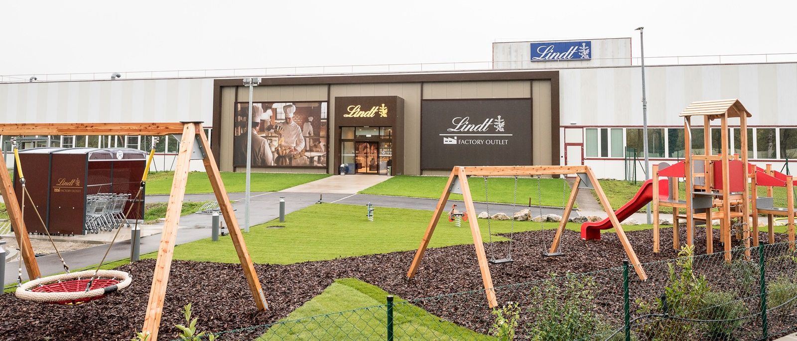 Playground in front of a Lindt Factory Outlet with swings and slide.