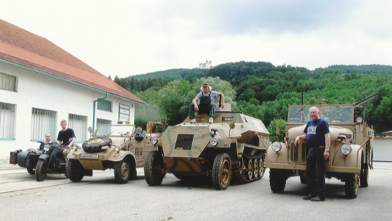 Military vehicles in front of a building with a hill in the background.