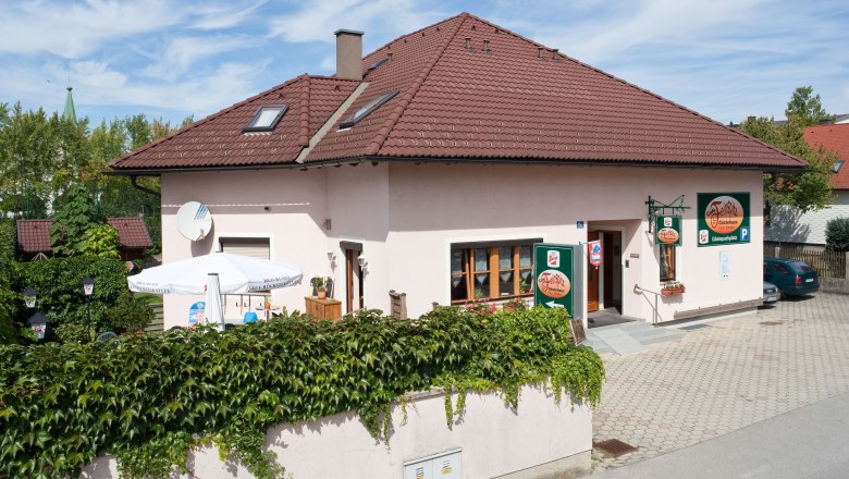 A guest house with a red roof and terrace, surrounded by green vegetation.