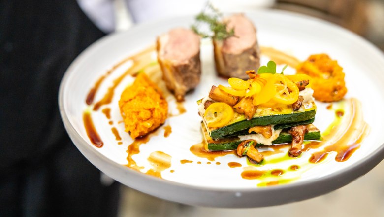 Gourmet dish on a white plate with meat, vegetables and sauce.