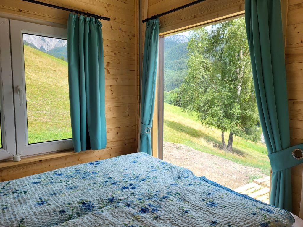 Interior view of a room with a bed and large windows offering a view of a green landscape.