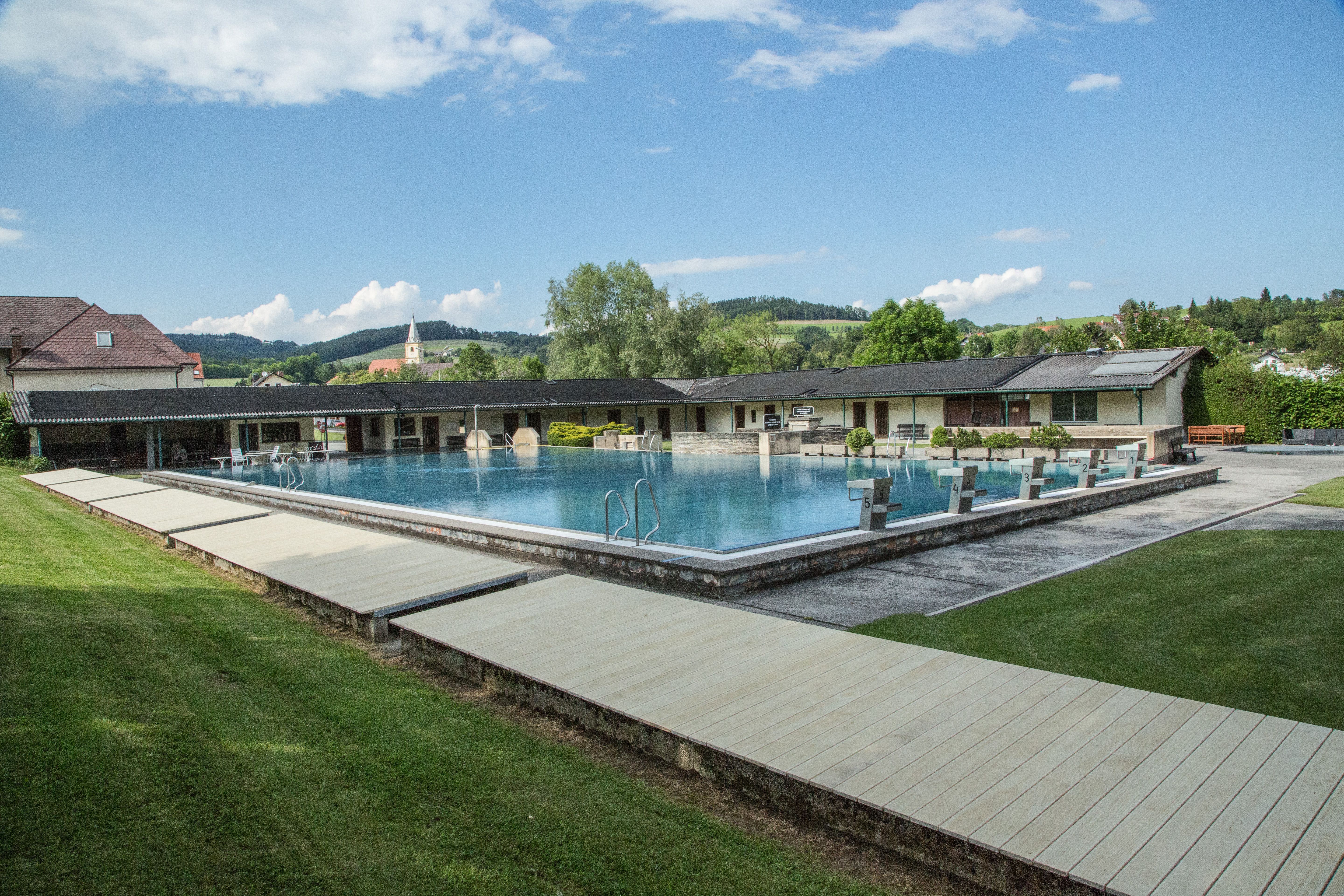 Krumbach outdoor pool with swimming pool and diving blocks, surrounded by green landscape and buildings.