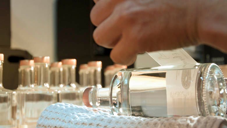 Close-up of a hand sticking a label on a bottle of brandy.