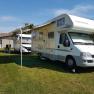 A white motorhome with an extended awning is parked on a meadow next to another vehicle.