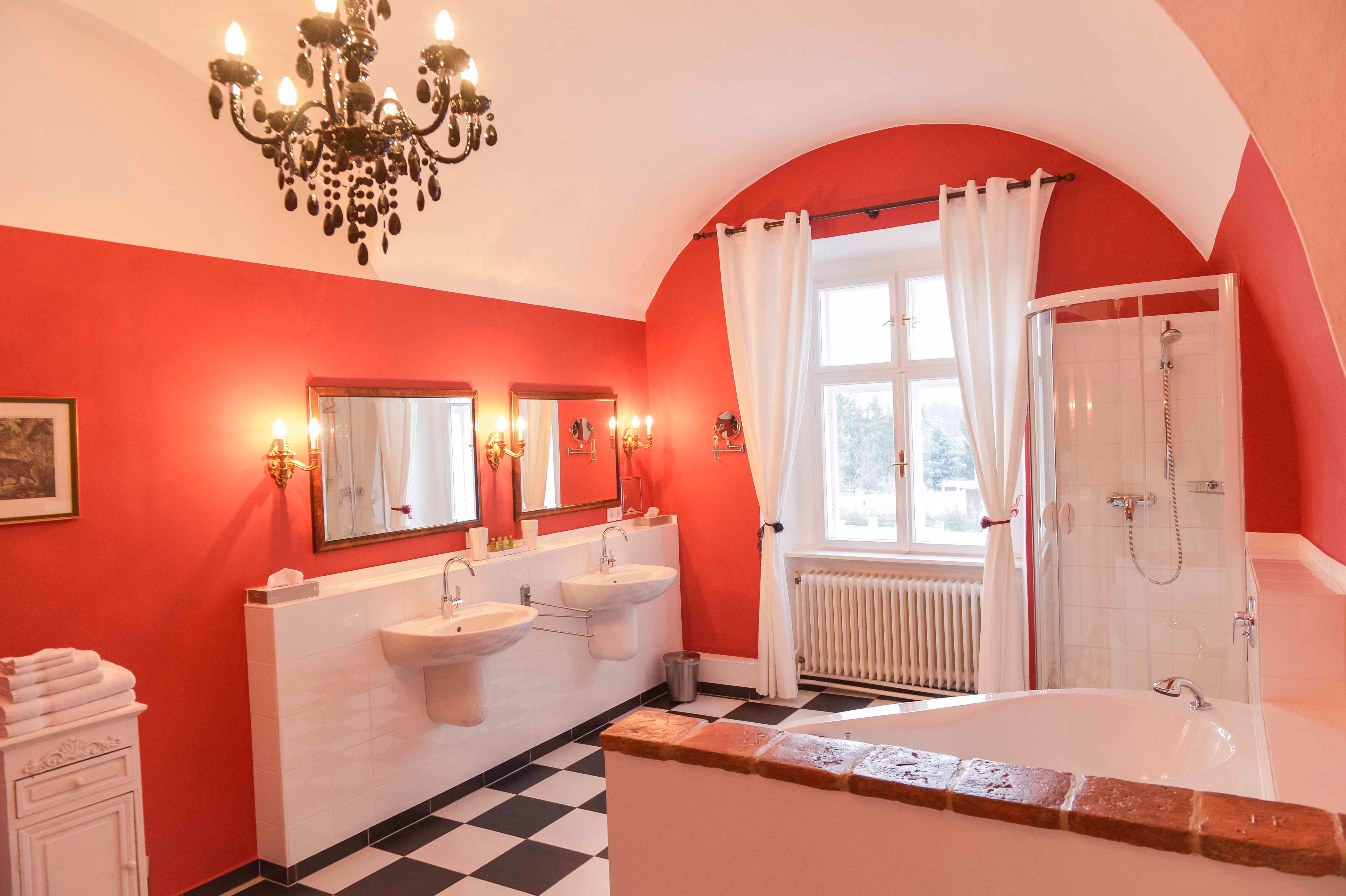 Elegant bathroom with red walls, two washbasins, bathtub, shower and chandelier.