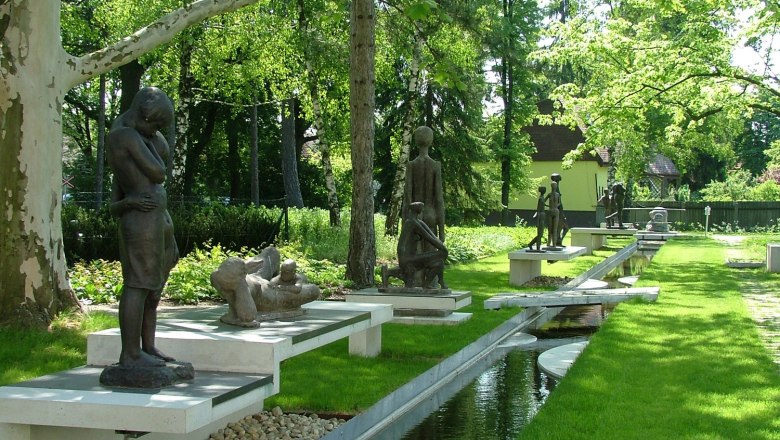 Outdoor sculptures in a green park with trees and a watercourse.