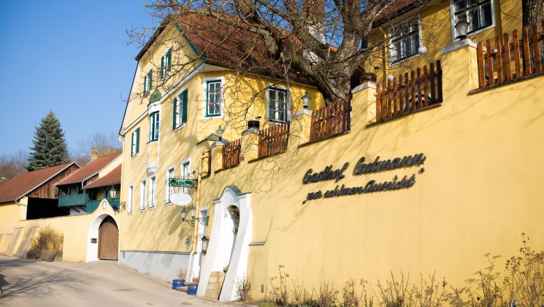 Yellow inn with green shutters and wooden fence, sunny day.
