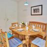 A cozy kitchen table with wooden chairs and blue cushions, set for four people, in a bright room with murals.
