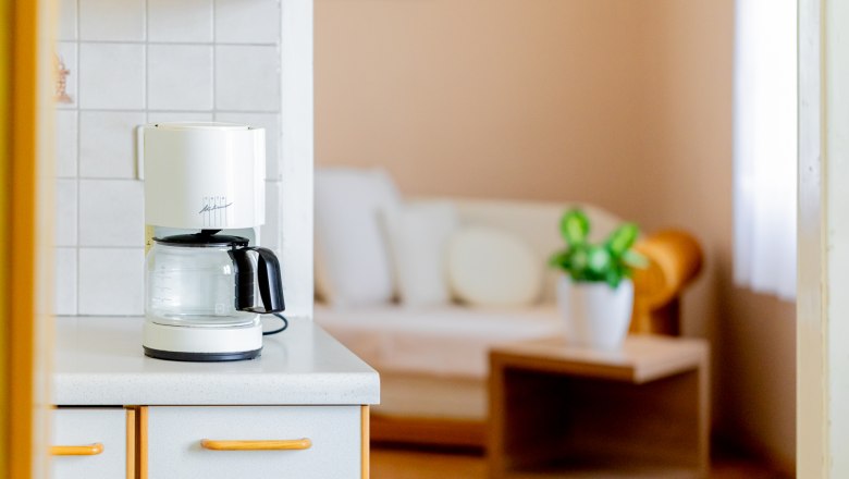Coffee machine on kitchen counter with living room in the background.
