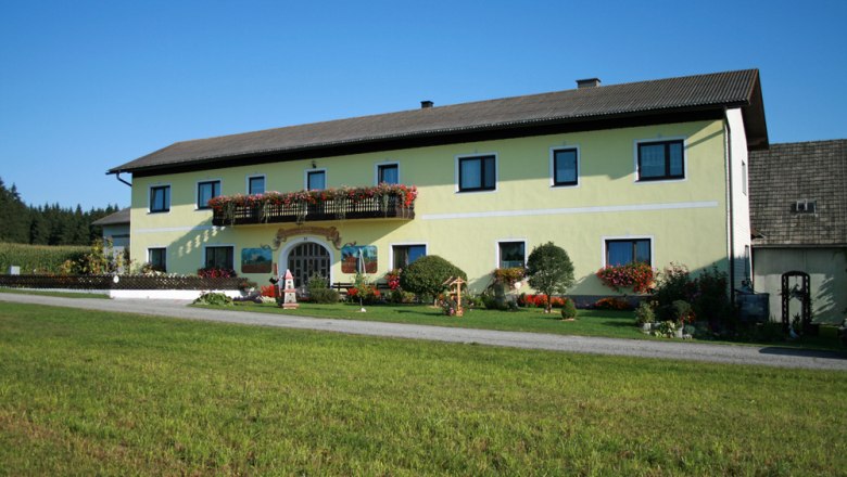 A yellow farmhouse with flowers and a green lawn in the foreground.