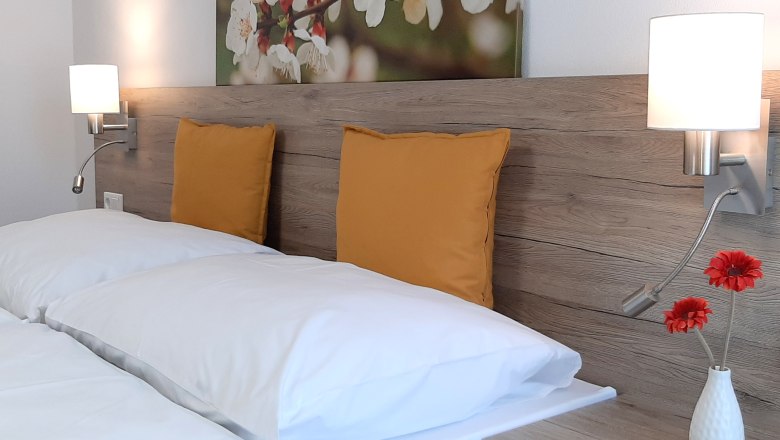 Double room, © Gerhard Auer Double bed with wooden back panel, yellow cushions and wall lamps.