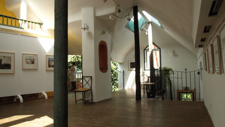 Interior view of a bright gallery with wooden floor, works of art on the walls and a person at the window.