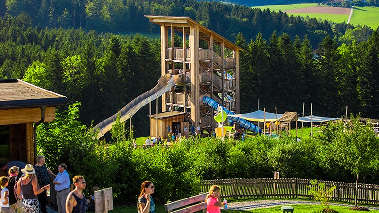 Wooden slide tower surrounded by trees, and people in the foreground.