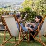 A couple sits in deckchairs in the garden and toasts with glasses of wine, overlooking a green landscape.