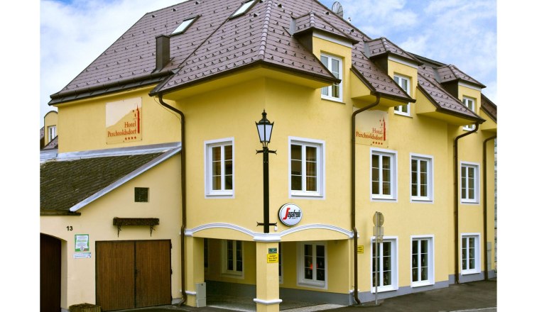 Yellow hotel building with several windows and a sign with the inscription 'Hotel Perchtoldsdorf'.