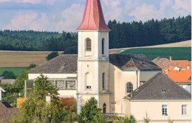Hochwolkersdorf parish church with red, pointed tower roof and surrounding landscape.