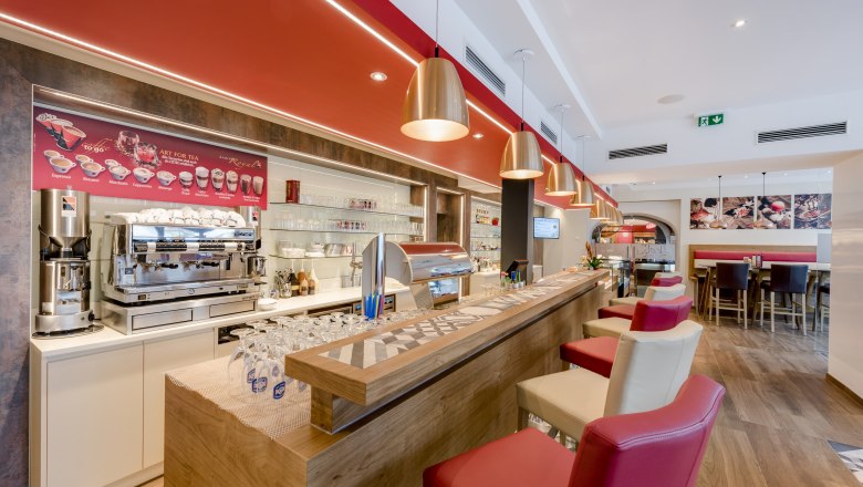 Interior view of a modern bistro with counter, coffee machine and bar stools.