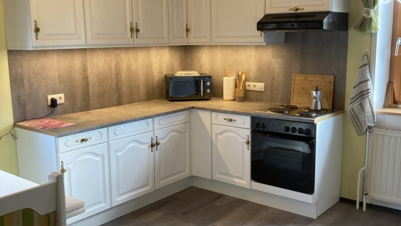 Spacious kitchen with white cupboards, stove, microwave and wooden ceiling.