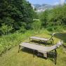 Two sun loungers on a meadow with a view of wooded mountains under a blue sky.