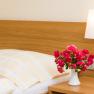 A guest room with a bed, a bedside lamp and a bouquet of flowers in a vase on the bedside table.