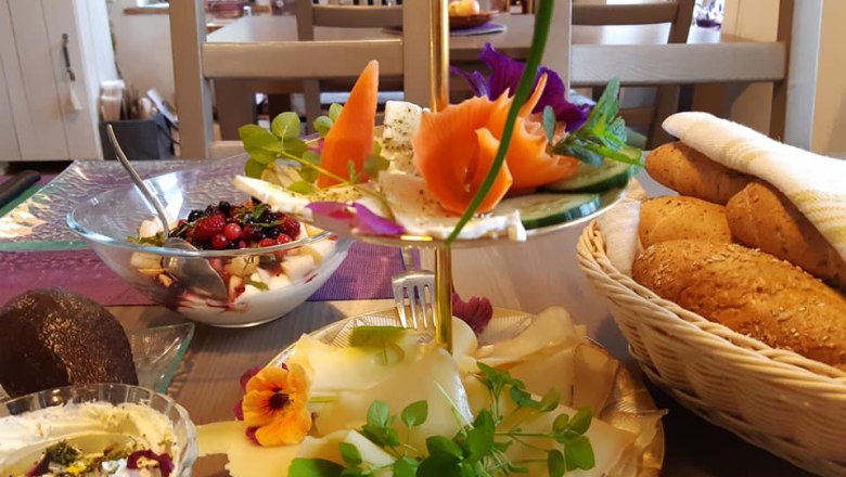 A laid breakfast table with bread rolls, cheese, yogurt with berries and decorative flowers.