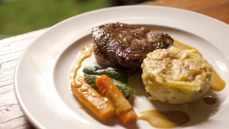 A plate with a piece of meat, vegetables and a potato side dish.
